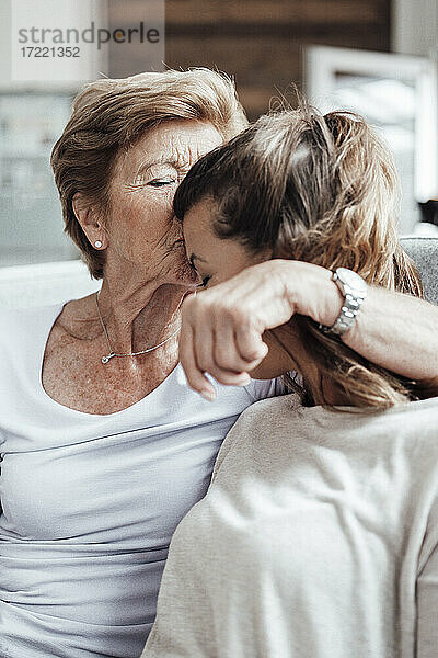 Fürsorgliche Großmutter küsst ihre Enkelin auf die Stirn  während sie zu Hause sitzt