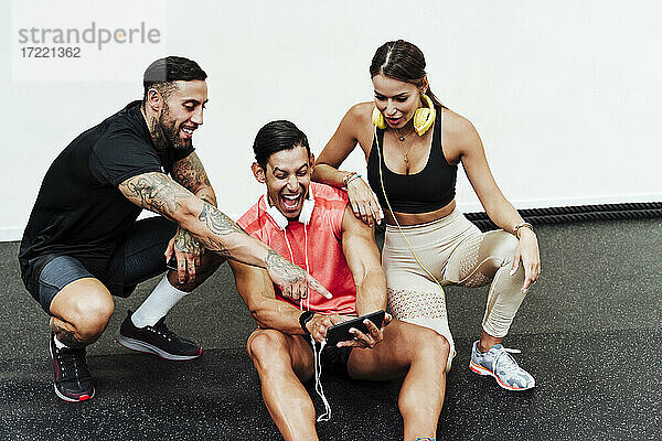 Sportler lachend bei der Benutzung eines Mobiltelefons durch Freunde im Fitnessstudio