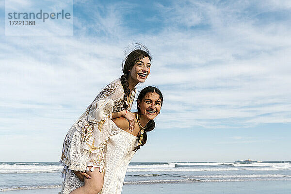 Verspielte Frau nimmt ihre Freundin am Strand huckepack