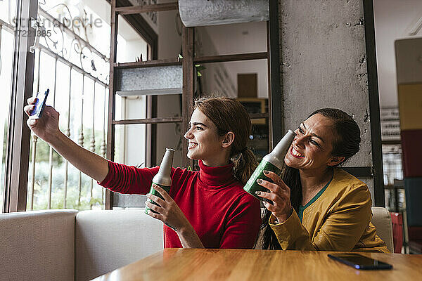 Fröhliche Freundinnen mit Bierflaschen machen ein Selfie mit dem Handy in einer Bar