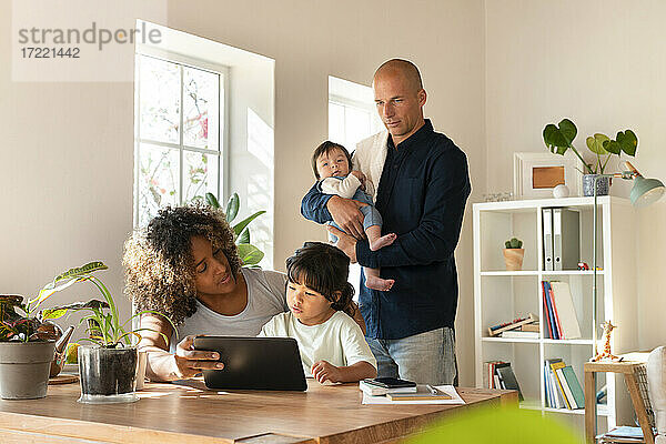 Familie mit kleinem Mädchen und Tochter  die zu Hause auf ein digitales Tablet schauen
