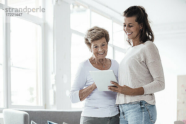 Lächelnde Großmutter und junge Frau schauen auf ein digitales Tablet