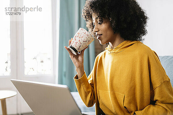 Frau trinkt Kaffee  während sie zu Hause am Laptop sitzt