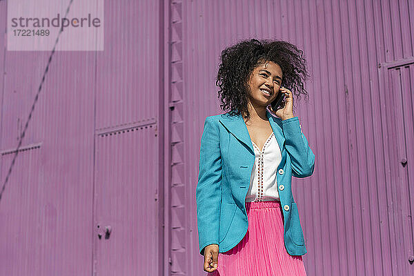 Lächelnde Frau mit Afrofrisur telefoniert an einem sonnigen Tag
