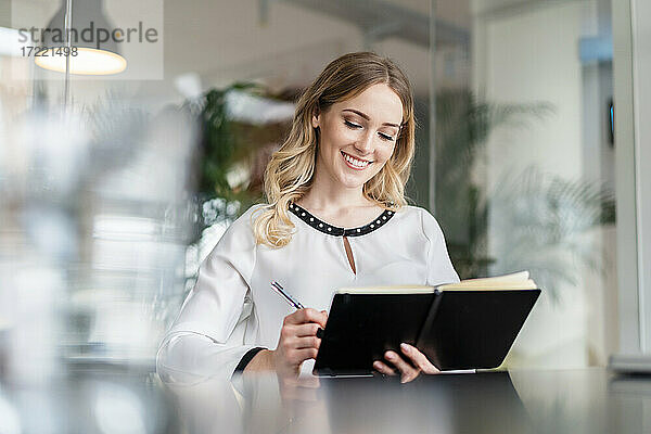 Lächelnde Geschäftsfrau  die im Büro in ihr Tagebuch schreibt