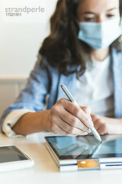 Geschäftsfrau mit digitalisiertem Stift bei der Arbeit auf einem digitalen Tablet in einem Café Pandemie
