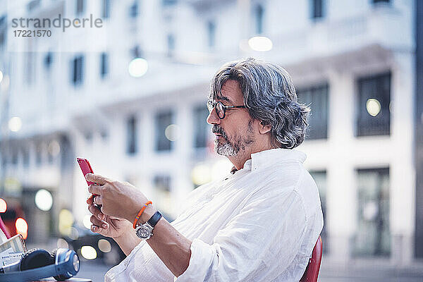 Attraktiver älterer Mann  der sein Smartphone benutzt  während er in einem Straßencafé in Madrid sitzt