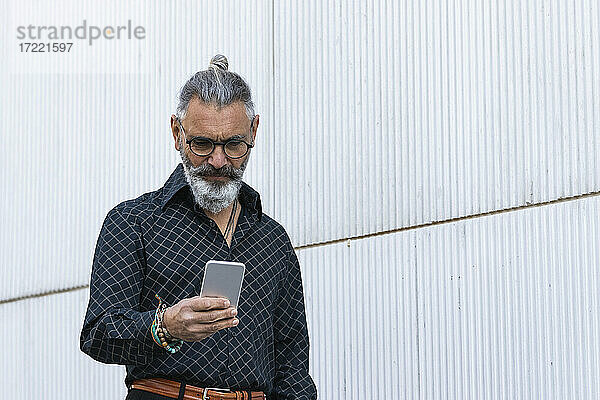 Hipster-Geschäftsmann mit Smartphone an der Wand