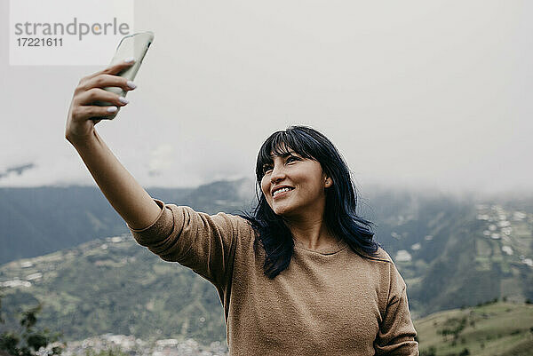 Lächelnd Mitte erwachsene Frau  die selfie durch Handy vor dem Himmel