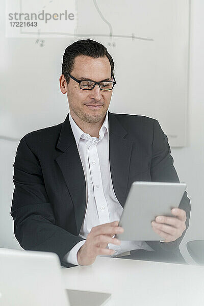 Männlicher Unternehmer  der am Arbeitsplatz sitzt und ein digitales Tablet benutzt