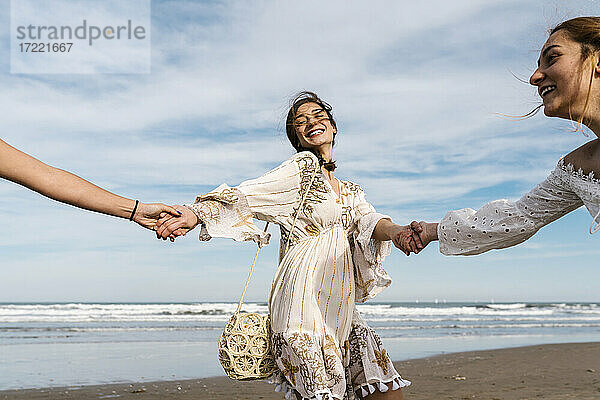 Glückliche Frau hält Hände von Freunden am Strand