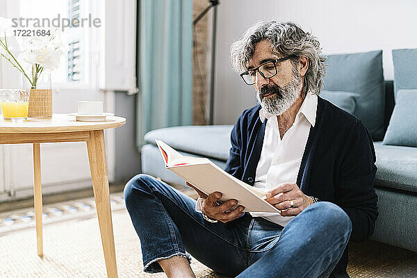 Älterer Mann liest ein Buch  während er zu Hause im Wohnzimmer sitzt