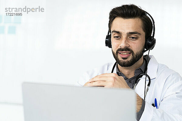 Ein männlicher Arzt trägt einen Kopfhörer  während er in einem Krankenhaus eine Videokonferenz abhält