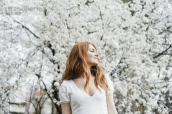 Junge Frau mit geschlossenen Augen vor einem weißen Mandelbaum stehend
