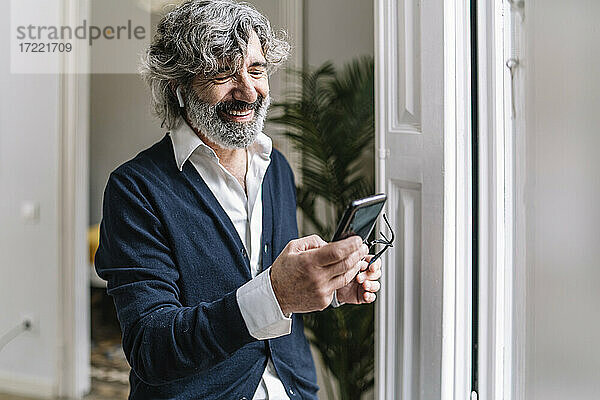 Lächelnder gut aussehender Mann  der zu Hause ein Smartphone benutzt