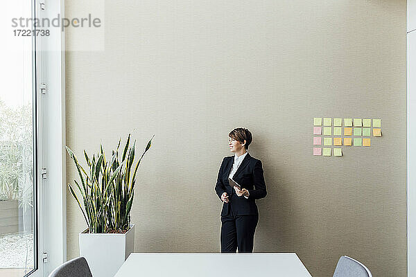 Betrachtung eines weiblichen Geschäftsmannes  der ein digitales Tablet hält  während er im Büro wegschaut