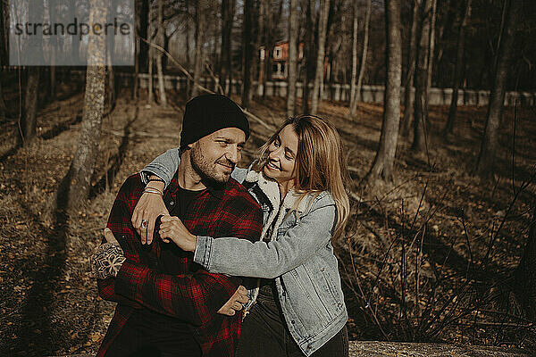 Lächelnde Frau mit Arm um Freund sitzt im Wald im Herbst