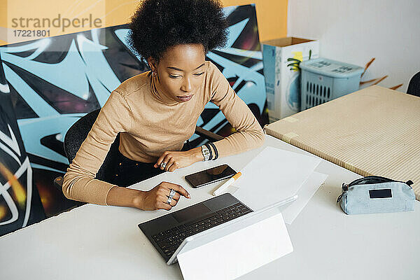 Junge Afro-Frau  die einen Laptop benutzt und am Tisch im Studio sitzt