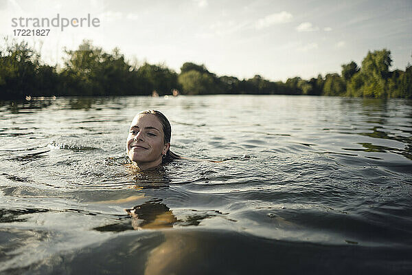 Junge Frau schwimmt im Sommer im See  lächelnd