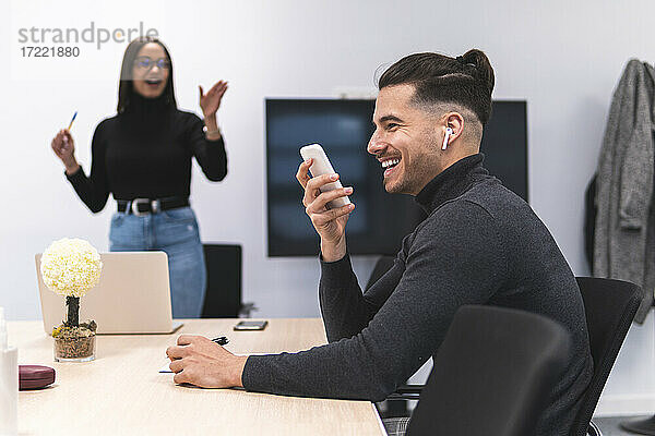 Lächelnder Geschäftsmann  der während einer Konferenz im Büro mit einem Mobiltelefon spricht