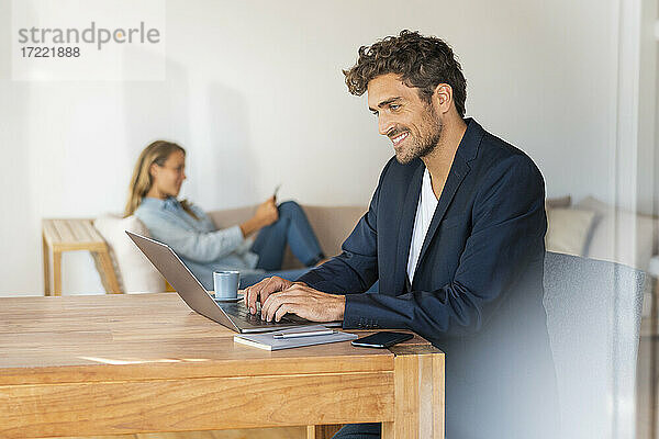 Mann benutzt Laptop auf dem Tisch  während seine Freundin zu Hause im Büro sitzt