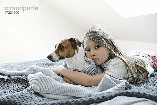 Nettes Mädchen umarmt Hund  während auf dem Bett zu Hause liegen