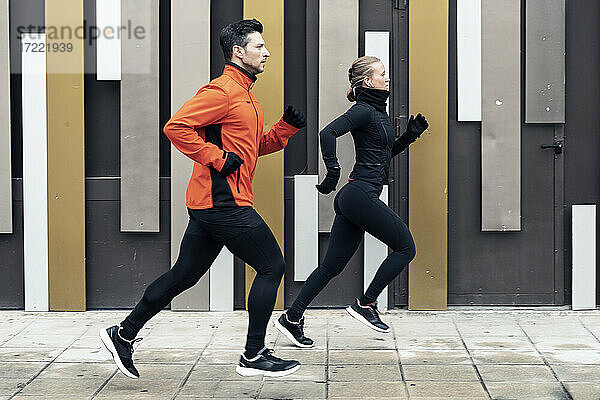 Entschlossene männliche und weibliche Freunde joggen auf dem Fußweg an der Mauer