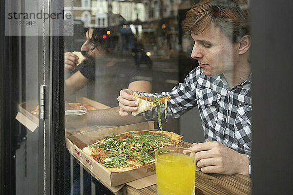 Geschäftsmann hält Pizzastück  während er am Tisch im Büro sitzt