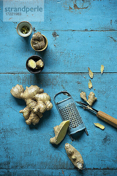 Ingwerwurzel  Reibe  kleine Tassen und Küchenmesser auf einer blauen Holzunterlage