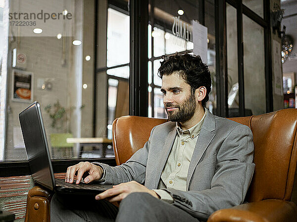 Lächelnder männlicher Unternehmer  der in einem Café am Laptop arbeitet