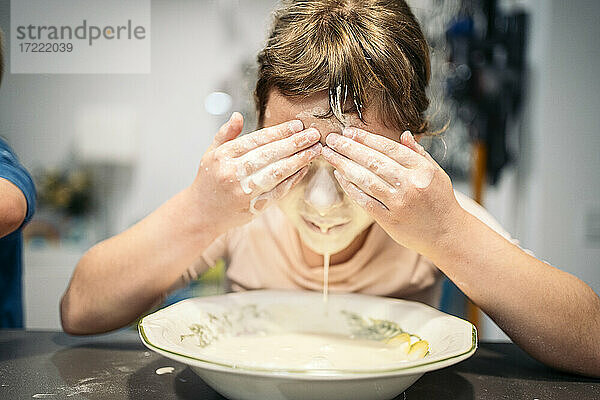 Mädchen  das die Augen mit den Händen bedeckt  während es sein Gesicht mit Mehl und Wasser beschmiert