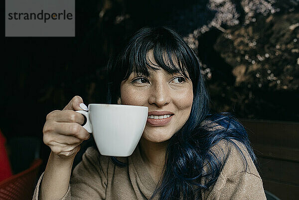 Lächelnde Frau träumt  während sie eine Kaffeetasse hält