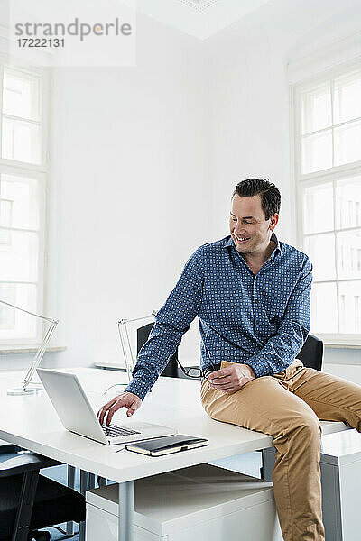 Männlicher Berufstätiger  der am Schreibtisch sitzt und einen Laptop am Arbeitsplatz benutzt