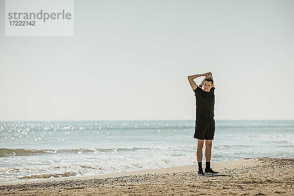 Junger Mann streckt die Hände aus  während er am Strand steht