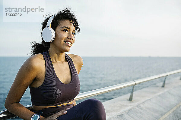 Nachdenkliche Sportlerin mit Kopfhörern auf einer Brücke sitzend