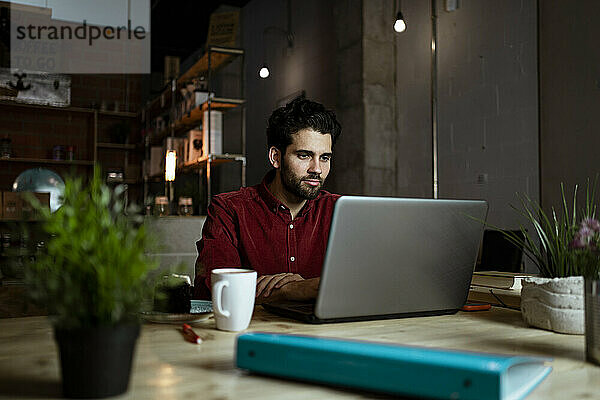 Mittlerer erwachsener männlicher Freiberufler mit Kaffeetasse  der in einem Café am Laptop arbeitet