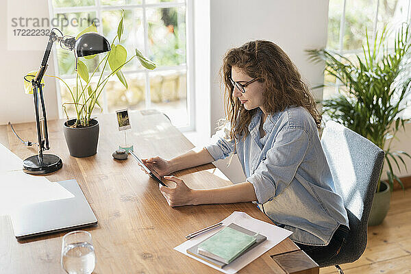 Junge Geschäftsfrau mit Brille schaut auf ein digitales Tablet im Heimbüro