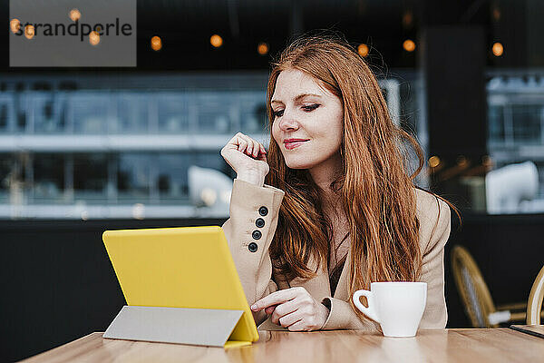 Rothaarige Frau schaut in einem Café auf eine digitale Tafel