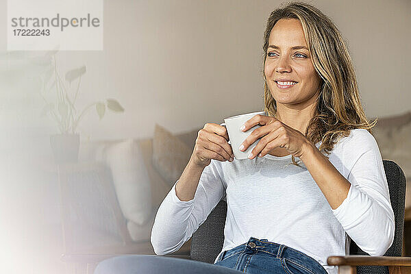 Lächelnde Frau  die wegschaut  während sie zu Hause Kaffee trinkt