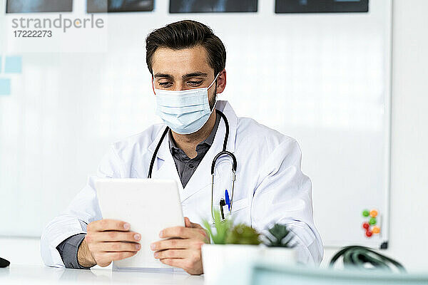Männlicher Arzt mit Gesichtsschutzmaske bei der Arbeit mit einem digitalen Tablet im Krankenhaus