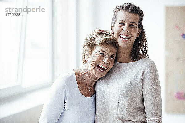 Fröhliche ältere Frau umarmt ihre Enkelin und lacht zu Hause