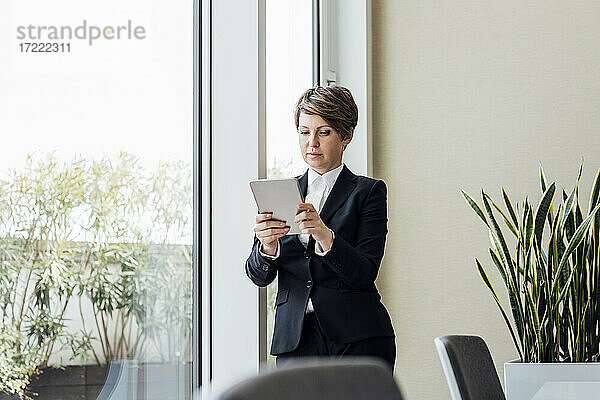 Unternehmerin  die ein digitales Tablet benutzt  während sie im Büro am Fenster steht