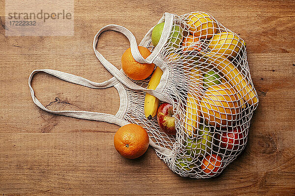 Wiederverwendbare Baumwoll-Netztasche mit frischen Früchten auf einem Holztisch liegend