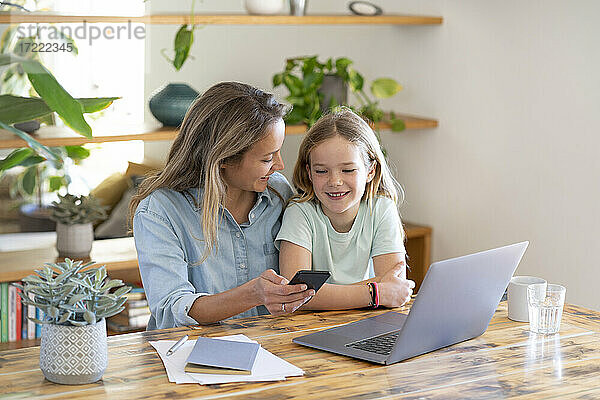 Geschäftsfrau und Tochter sitzen mit Laptop und Smartphone am Tisch