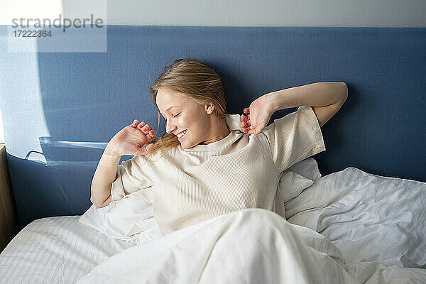 Lächelnde Frau  die ihre Hand ausstreckt  während sie zu Hause auf dem Bett liegt