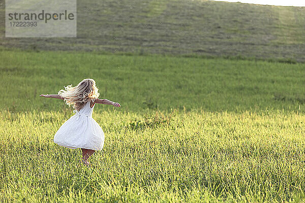 Blondes Mädchen tanzt bei Sonnenuntergang auf einer Wiese