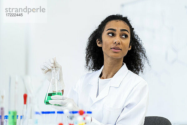 Junge Ärztin  die einen Flüssigkeitskolben hält  während sie im Labor wegschaut