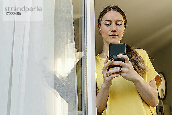 Mid adult woman using smart phone while leaning on window
