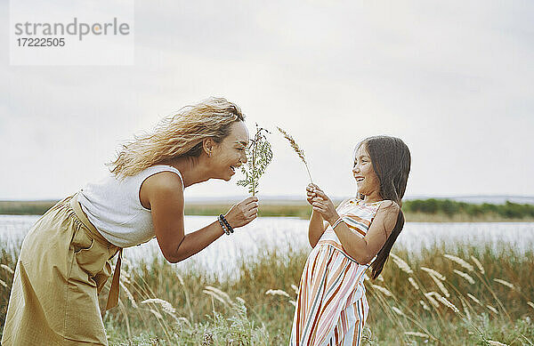 Verspielte Mutter und Tochter halten Zweige am See