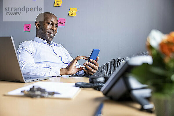 Männlicher Unternehmer mit Smartphone am Schreibtisch im Büro